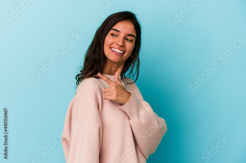 Young caucasian woman isolated on blue background looks aside smiling, cheerful and pleasant.