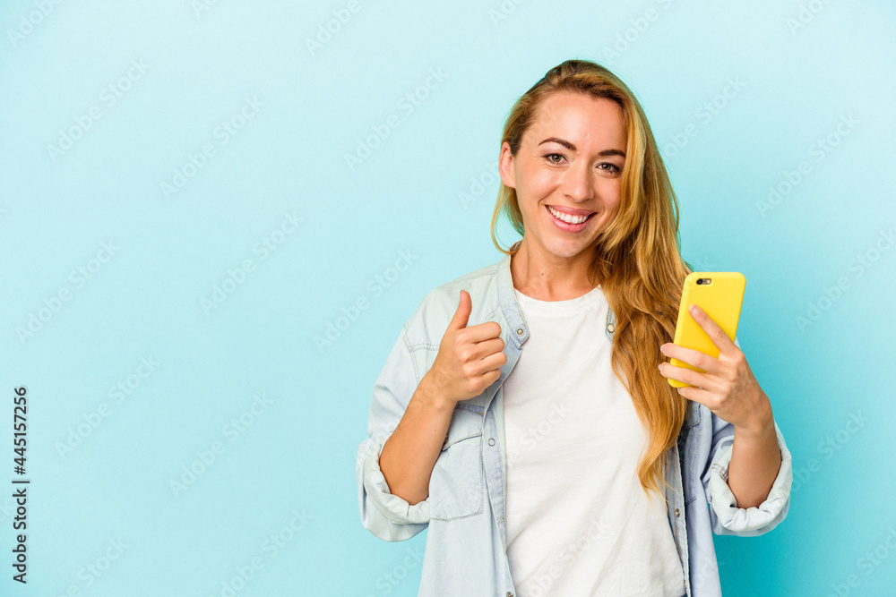 Caucasian woman holding mobile phone isolated on blue background smiling and raising thumb up