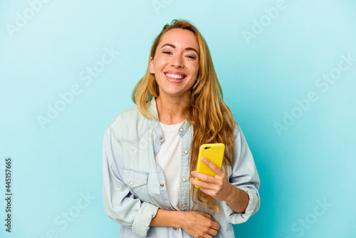 Caucasian woman holding mobile phone isolated on blue background laughing and having fun.