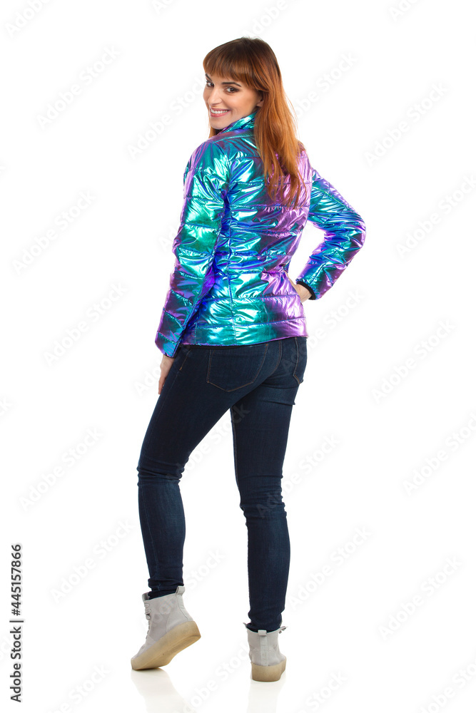 Young Woman In Vibrant Down Jacket Is Looking At Camera Over The Shoulder. Rear View. Young Woman In Vibrant Down Jacket Is Looking At Camera Over The Shoulder. Rear View.