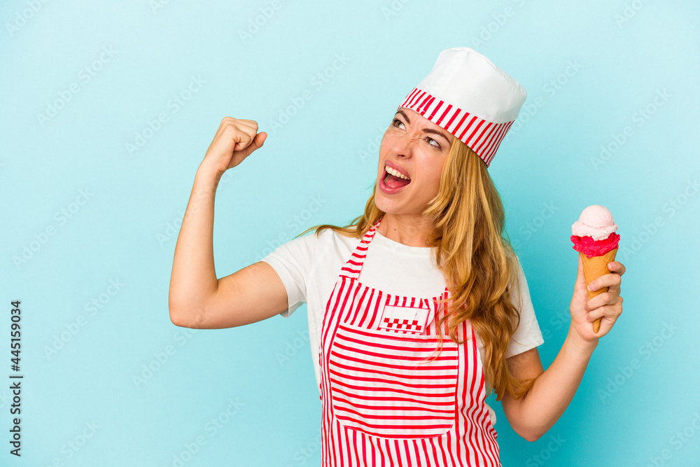 Caucasian ice cream maker woman holding an ice cream isolated on blue background raising fist after a victory, winner concept. Caucasian ice cream maker woman holding an ice cream isolated on blue background raising fist after a victory, winner concept.