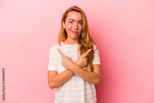 Caucasian blonde woman isolated on pink background points sideways, is trying to choose between two options.