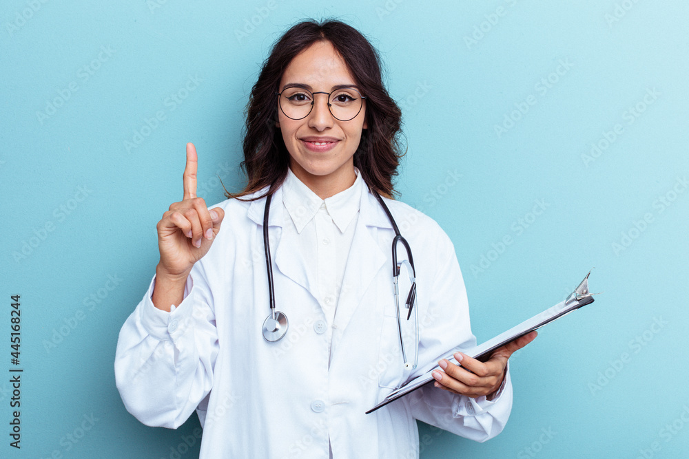 Young doctor mexican woman isolated on blue background showing number one with finger. Young doctor mexican woman isolated on blue background showing number one with finger.