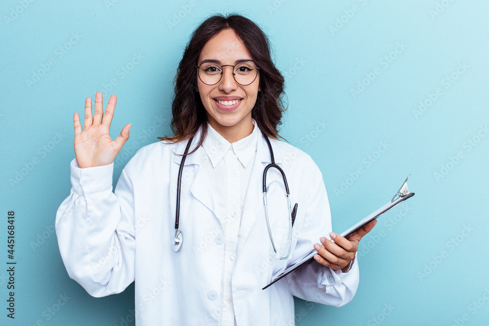 Young doctor mexican woman isolated on blue background smiling cheerful showing number five with fingers. Young doctor mexican woman isolated on blue background smiling cheerful showing number five with fingers.