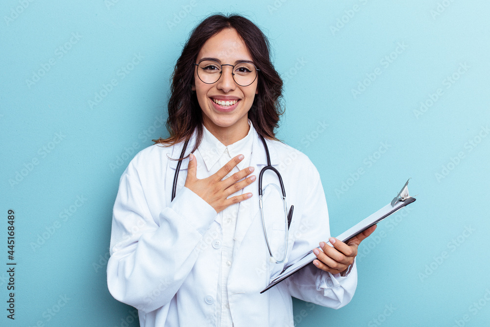 Young doctor mexican woman isolated on blue background laughs out loudly keeping hand on chest. Young doctor mexican woman isolated on blue background laughs out loudly keeping hand on chest.
