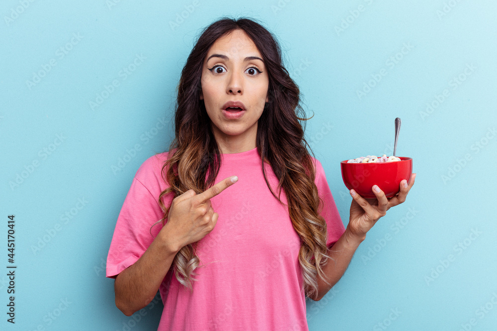 Young mixed race woman holding cereals bowl isolated on blue background pointing to the side Young mixed race woman holding cereals bowl isolated on blue background pointing to the side