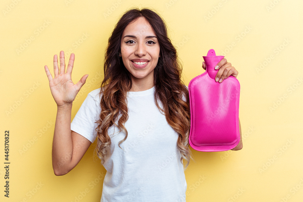 Young mixed race woman holding a hot bag isolated on yellow background smiling cheerful showing number five with fingers. Young mixed race woman holding a hot bag isolated on yellow background smiling cheerful showing number five with fingers.