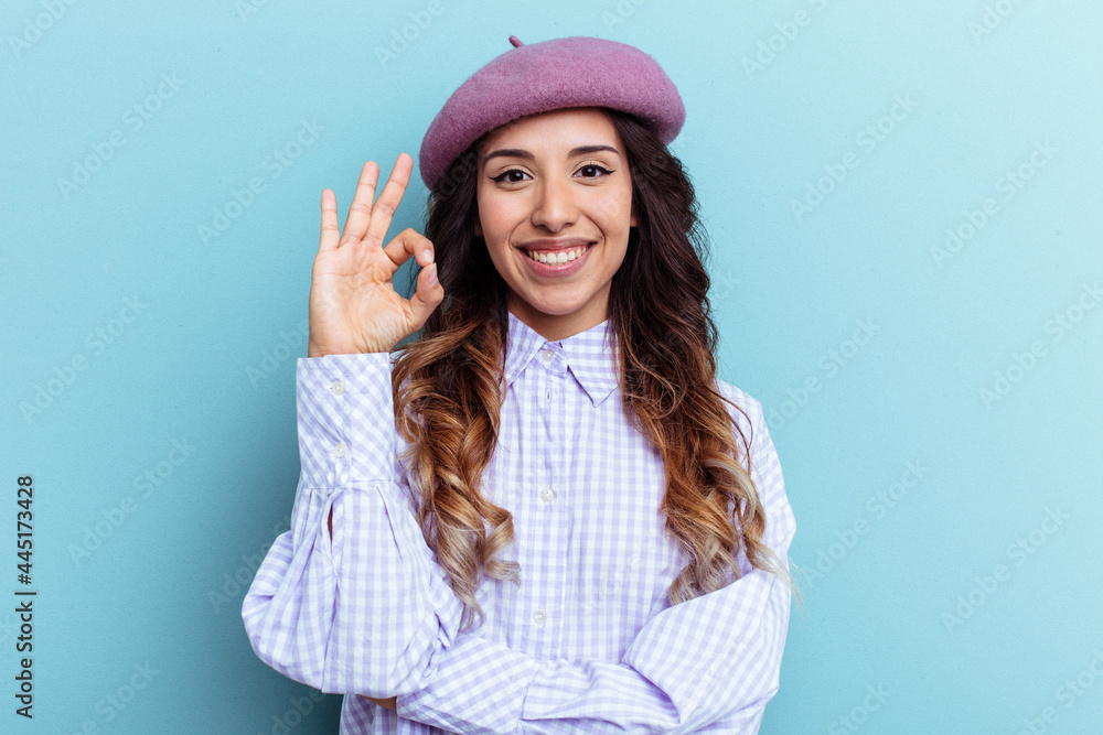 Young mexican woman isolated on blue background winks an eye and holds an okay gesture with hand. Young mexican woman isolated on blue background winks an eye and holds an okay gesture with hand.