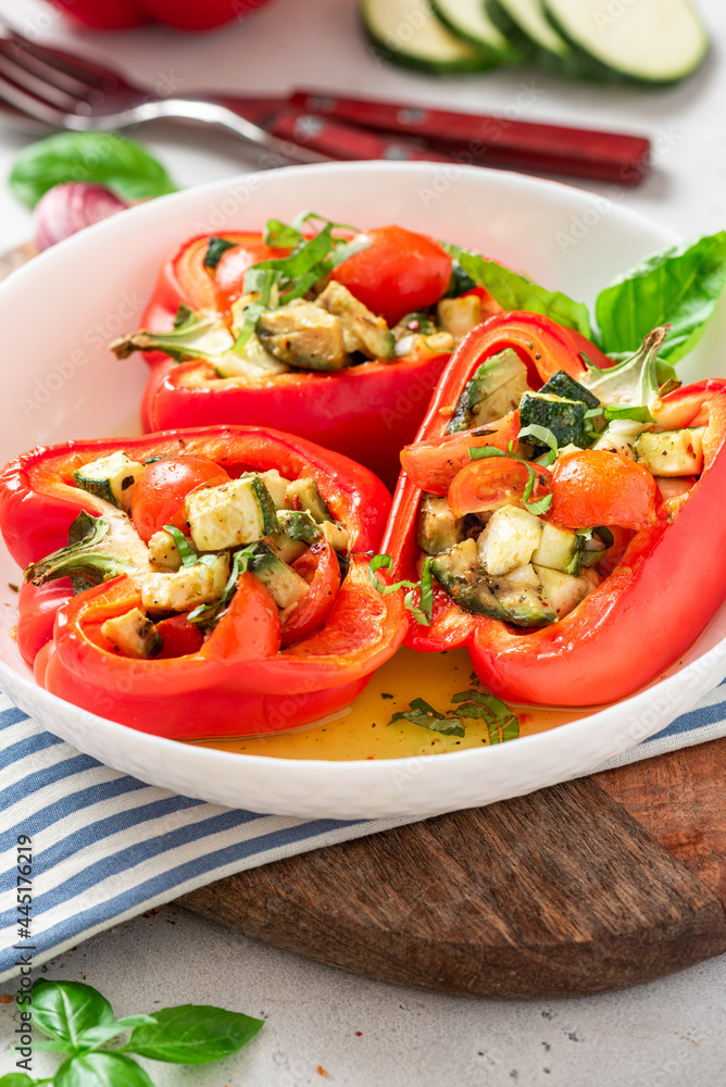Baked peppers stuffed with vegetables in a plate on a gray concrete background. Baked peppers with zucchini, avocado, tomatoes and basil. Vegan or diet food. Baked peppers stuffed with vegetables in a plate on a gray concrete background. Baked peppers with zucchini, avocado, tomatoes and basil. Vegan or diet food.