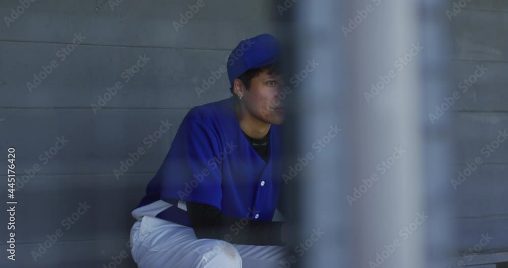 Nervous mixed race female baseball player, sitting on bench waiting, holding baseball bal Nervous mixed race female baseball player, sitting on bench waiting, holding baseball bal