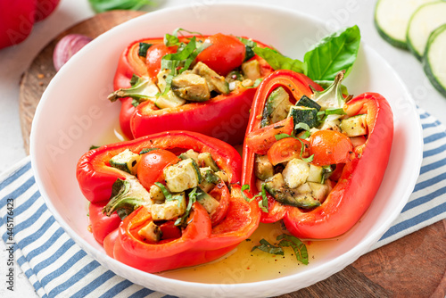 Baked peppers stuffed with vegetables in a plate on a gray concrete background. Baked peppers with zucchini, avocado, tomatoes and basil. Vegan or diet food.