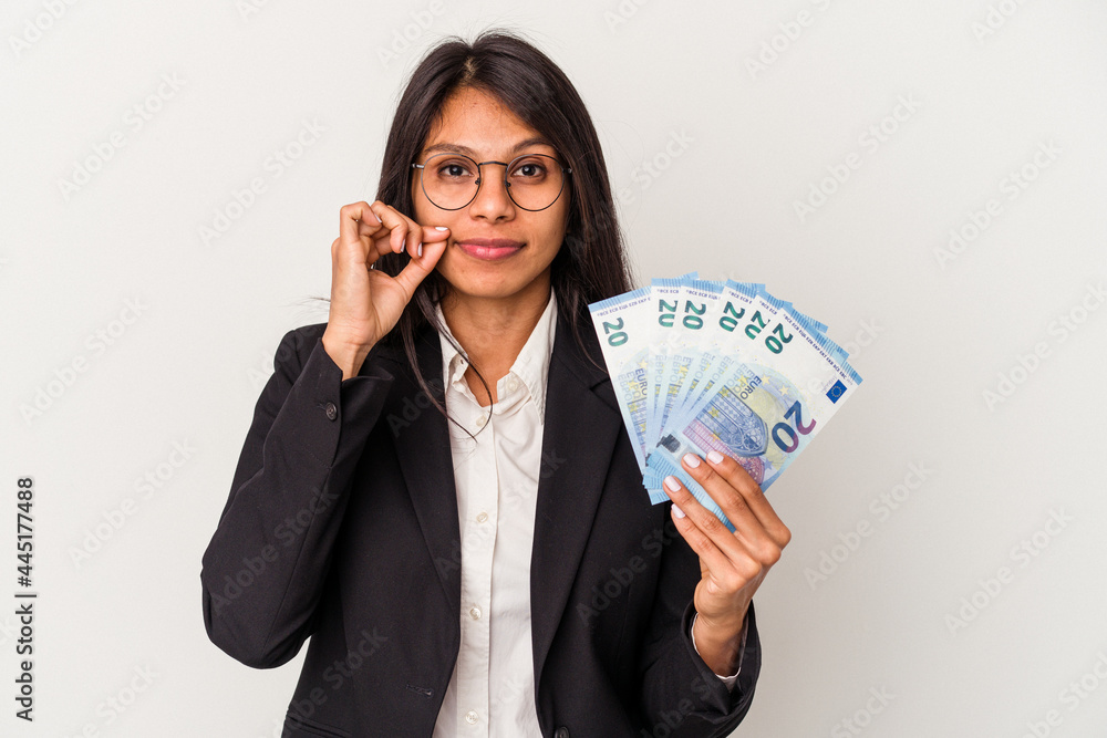 Young business latin woman holding bills isolated on white background with fingers on lips keeping a secret. Young business latin woman holding bills isolated on white background with fingers on lips keeping a secret.