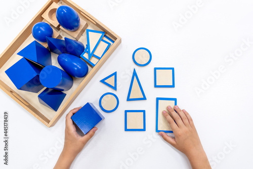 Top view of girls hand is sorting a puzzle of colored wooden geometric shapes in montessori school.