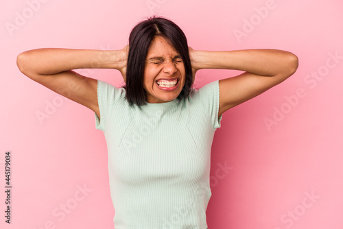 Young latin woman isolated on pink background covering ears with hands trying not to hear too loud sound.