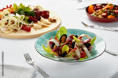 Mussels vongole with salad, mussels cooked in white wine sauce, mussel appetizer on the table surrounded by a selection of cheeses and other snacks