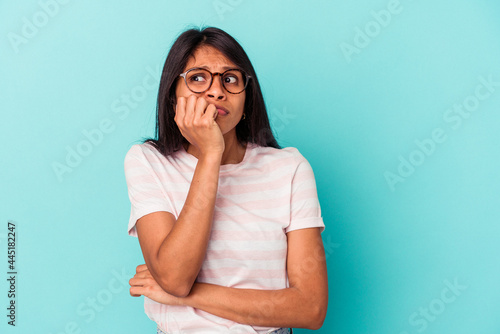 Young latin woman isolated on blue background biting fingernails, nervous and very anxious.