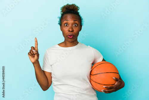 Young african american woman playing basketball isolated on blue background having some great idea, concept of creativity. © Asier
