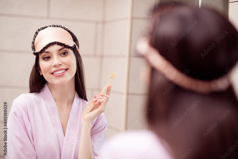Photo of adorable shiny young woman pink nightwear looking mirror brushing teeth smiling indoors home room Photo of adorable shiny young woman pink nightwear looking mirror brushing teeth smiling indoors home room