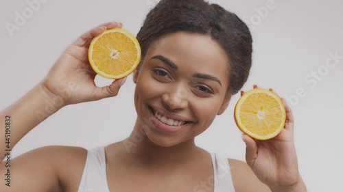 Vitamin C for skin. Young pretty african american lady deviding orange on two halves and smiling to camera with it photo