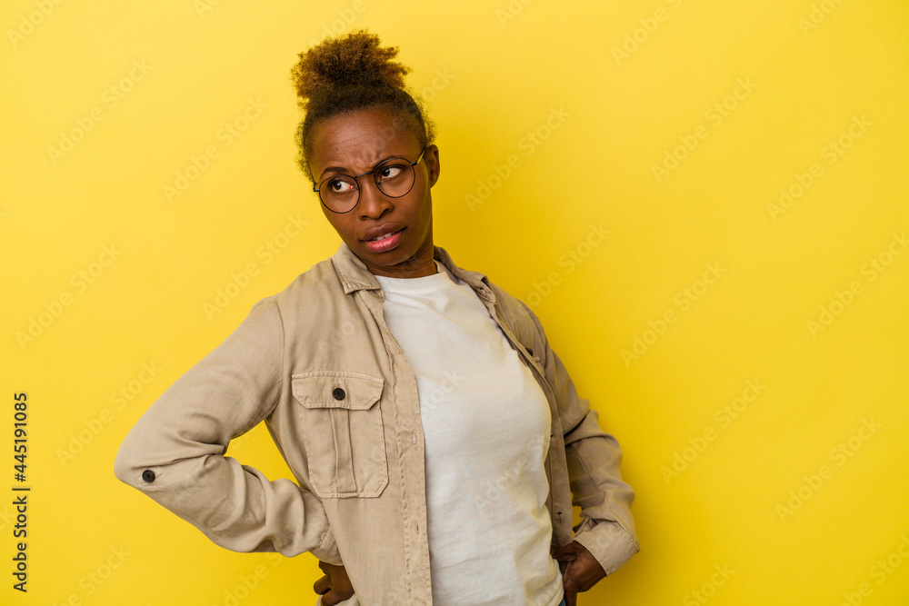 Young african american woman isolated on yellow background looks aside smiling, cheerful and pleasant. Young african american woman isolated on yellow background looks aside smiling, cheerful and pleasant.