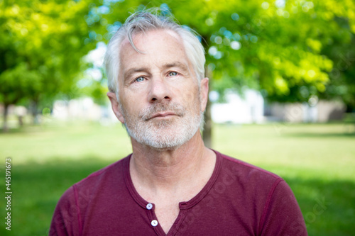 Handsome grey haired man in maroon shirt facing camera in park