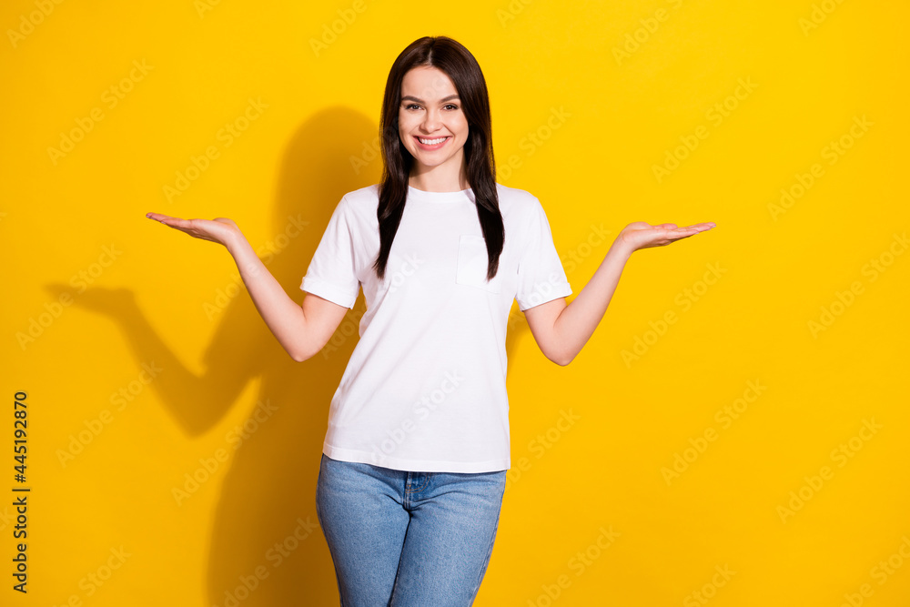 Photo of adorable cute young lady dressed white t-shirt showing scales holding arms empty space isolated yellow color background Photo of adorable cute young lady dressed white t-shirt showing scales holding arms empty space isolated yellow color background