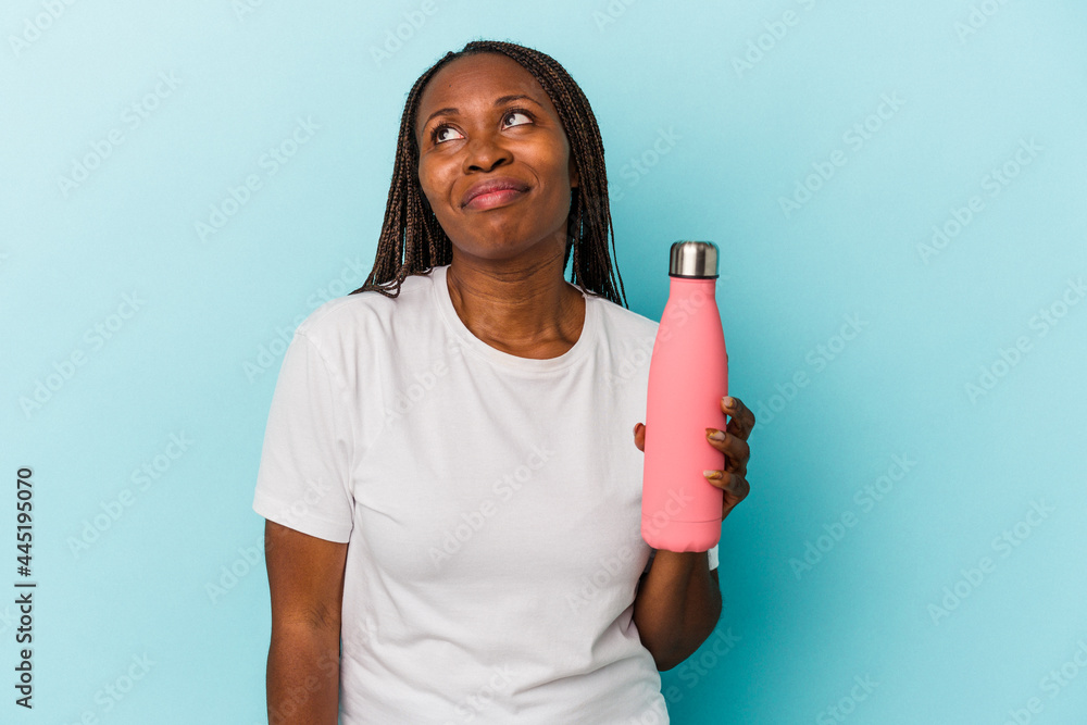 Young african american woman holding canteen isolated on blue background dreaming of achieving goals and purposes Young african american woman holding canteen isolated on blue background dreaming of achieving goals and purposes