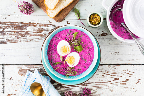 Cold soup made from beets, cucumbers and garnished with an egg in a blue plate on a wooden background. Top view.