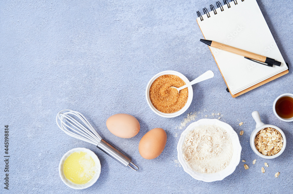 Healthy Food Background, Ingredients for homemade oat pancake with whole grain oat, coconut sugar, vanilla syrup, organic eggs next to a white notebook in a pen on light blue background. Copy space. Healthy Food Background, Ingredients for homemade oat pancake with whole grain oat, coconut sugar, vanilla syrup, organic eggs next to a white notebook in a pen on light blue background. Copy space.