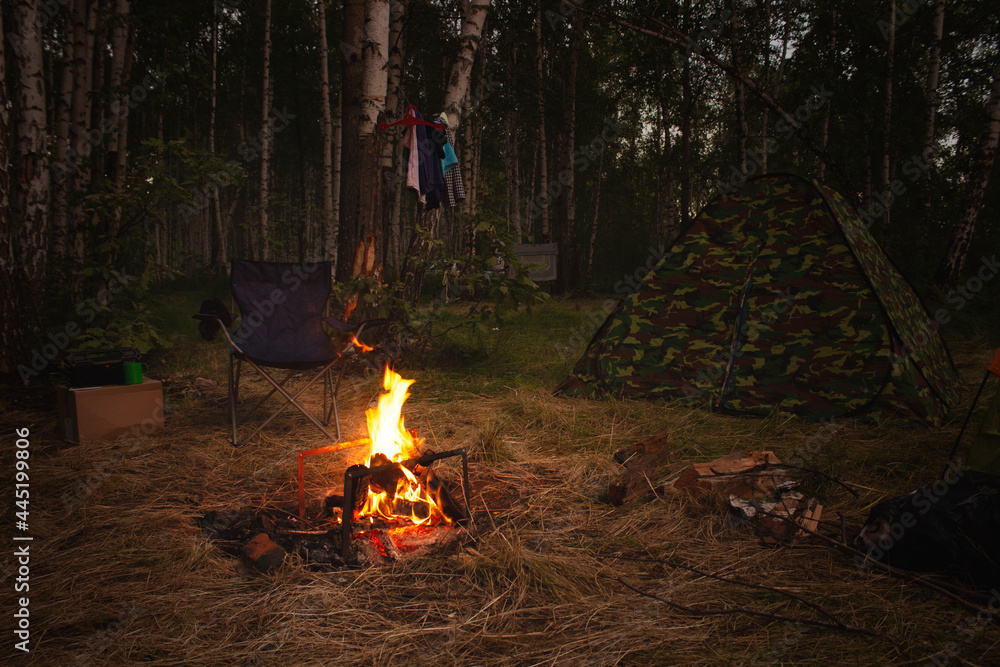 Night camp in the forest with a campfire. A tent with a fire and a chair in the evening in the forest. Outdoor recreation