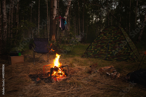 Fototapeta Naklejka Na Ścianę i Meble -  Night camp in the forest with a campfire. A tent with a fire and a chair in the evening in the forest. Outdoor recreation