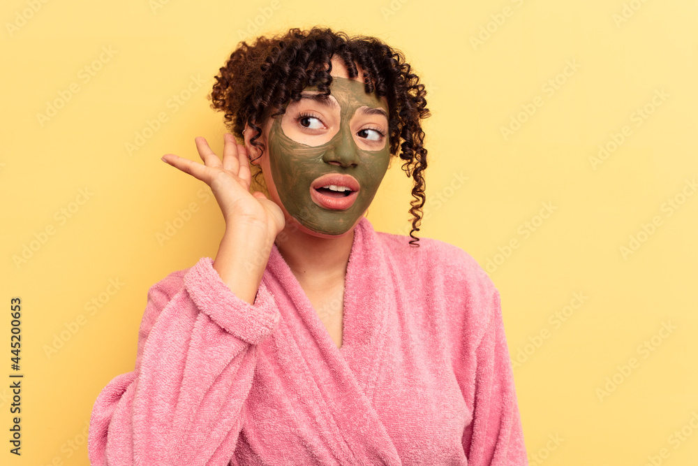 Young mixed race wearing facial mask isolated on yellow background trying to listening a gossip. Young mixed race wearing facial mask isolated on yellow background trying to listening a gossip.