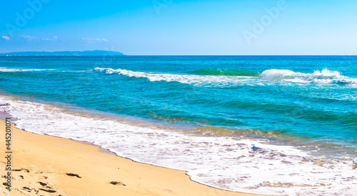 Blue sea with a foamy wave and a sandy beach. Summer panorama of nature