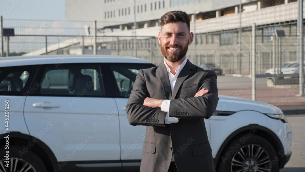 Confident bearded businessman with toothy smile posing foe the camera crossed arms in the parking near white car background. Young millennial man looking on the camera. Successful people concept. Confident bearded businessman with toothy smile posing foe the camera crossed arms in the parking near white car background. Young millennial man looking on the camera. Successful people concept.