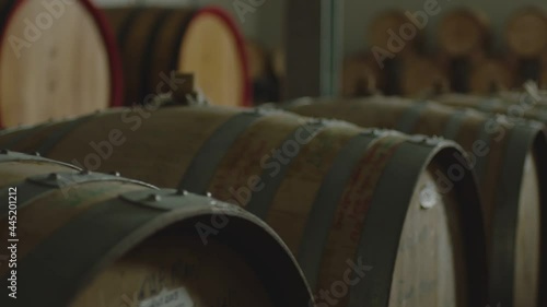 Aged wooden barrels with a wine , brandy or whiskey in a big warehouse . Dolly , gimbal movement a long row of wine barrels at a vintage winery with alcohol . Wine preparation and fermenting process