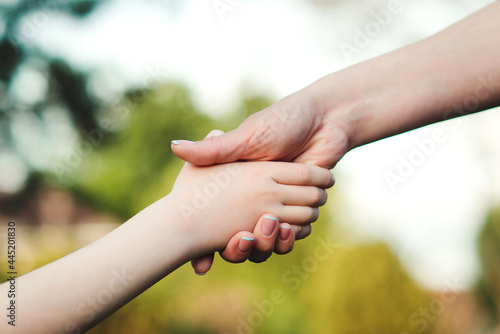 Mother and child hands on nature background. Family support, help and trust.