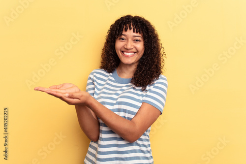 Young mixed race woman isolated on yellow background holding a copy space on a palm.