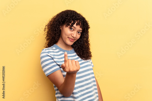 Young mixed race woman isolated on yellow background pointing with finger at you as if inviting come closer.