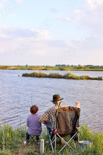 senior man with teenage boy relaxing at lakeside, going to fish. rear view .family, generation, summer holidays and people concept. happy child enjoy spending time with grandfather