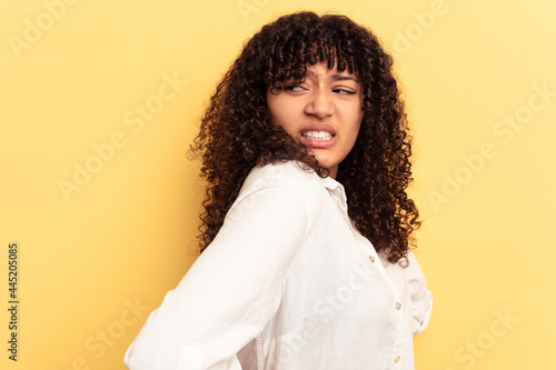 Young mixed race woman isolated on yellow background suffering a back pain. © Asier