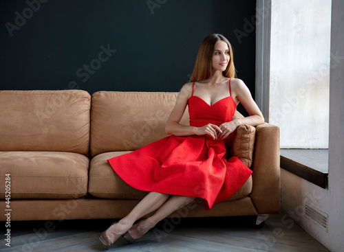 young woman sits on the sofa and looks out the window, portrait of a beautiful girl