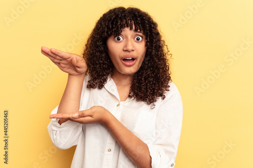 Young mixed race woman isolated on yellow background holding something with both hands, product presentation.