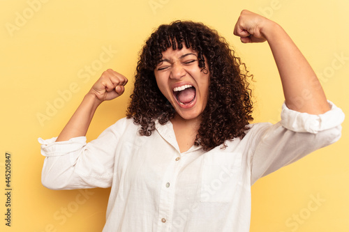 Young mixed race woman isolated on yellow background raising fist after a victory, winner concept.