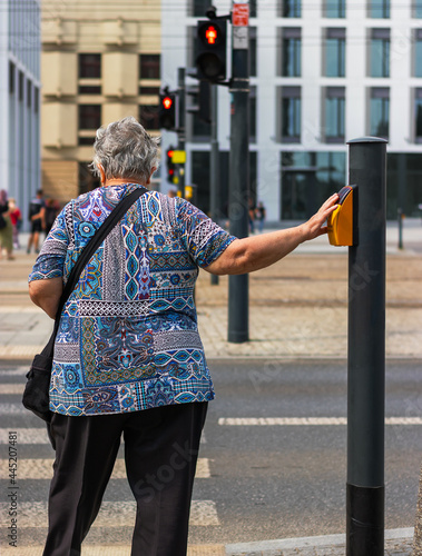 An elderly woman stands at a traffic light in a close-up