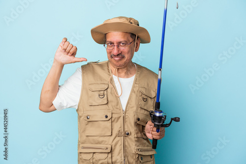 Senior indian fisherman holding rod isolated on blue background feels proud and self confident, example to follow.