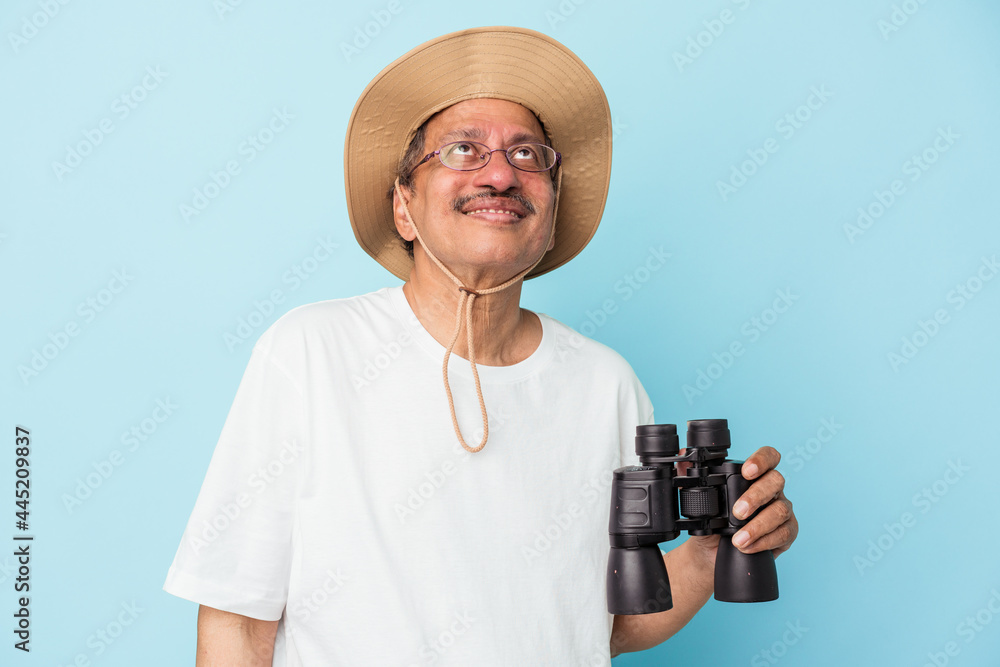 Middle aged indian fisherman holding rod isolated on blue background dreaming of achieving goals and purposes Middle aged indian fisherman holding rod isolated on blue background dreaming of achieving goals and purposes