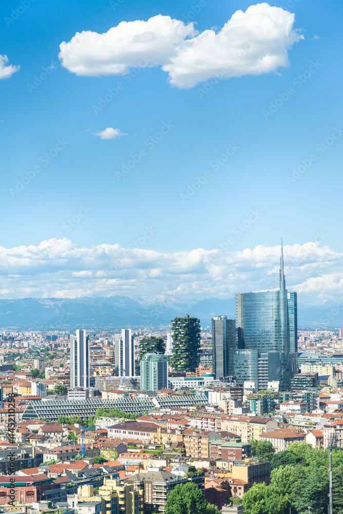 Obraz premium Vertical aerial view of Milan skyline, Italy, with business skyscrapers. In the distance the alps mountain range is visible. Blue sky and white clouds on the background.