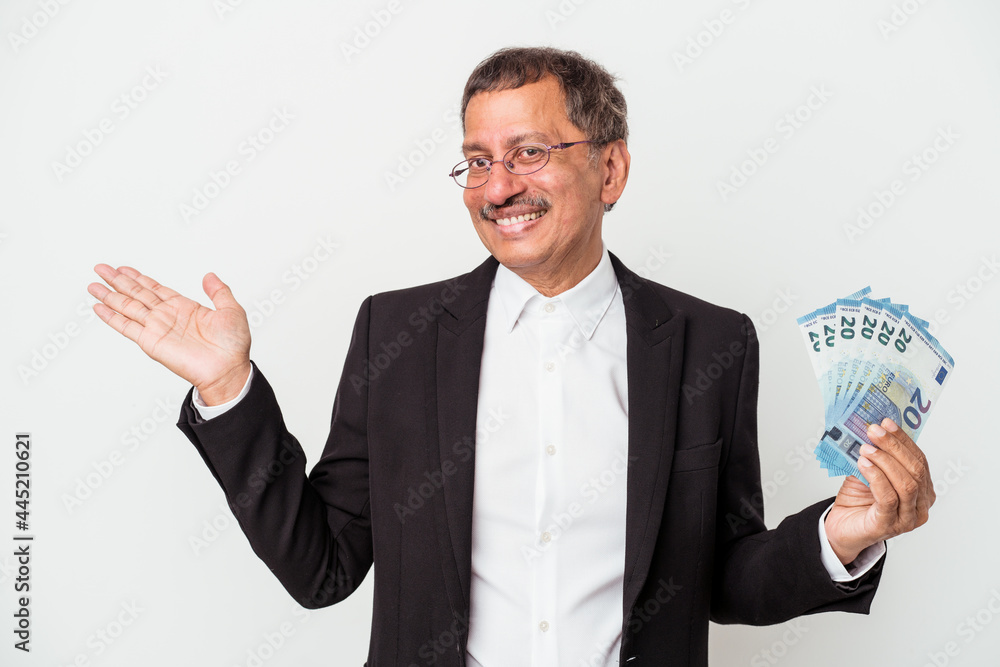Middle aged indian business man holding bills isolated on white background showing a copy space on a palm and holding another hand on waist. Middle aged indian business man holding bills isolated on white background showing a copy space on a palm and holding another hand on waist.