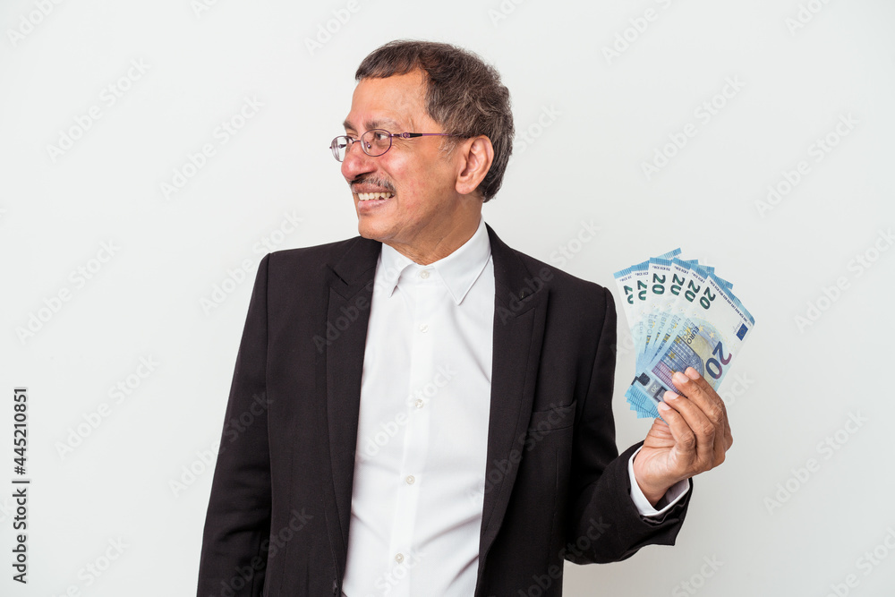 Middle aged indian business man holding bills isolated on white background looks aside smiling, cheerful and pleasant. Middle aged indian business man holding bills isolated on white background looks aside smiling, cheerful and pleasant.