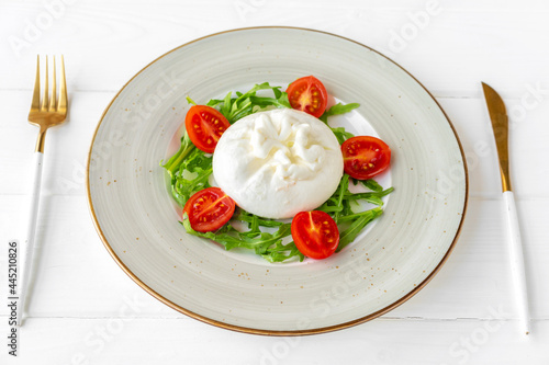 Salad with burrata cheese and cherry tomatoes on white wooden background